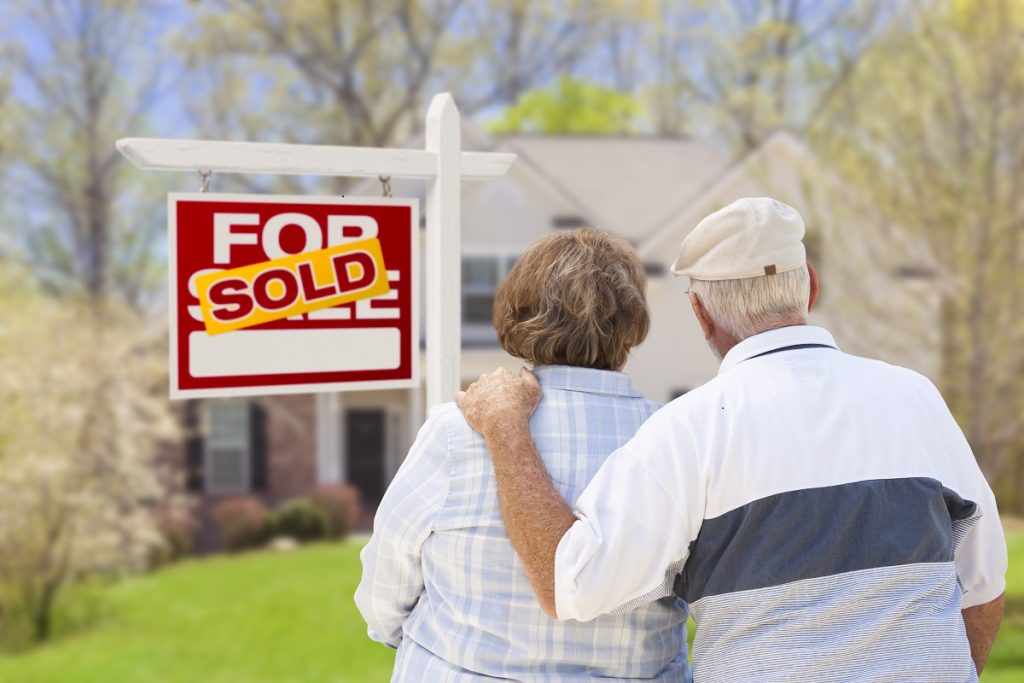 senior couple hugging in front of sold house